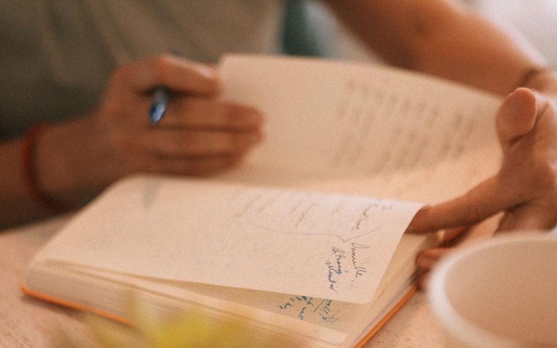 Hands turning pages of an open cream journal on a warm wood table